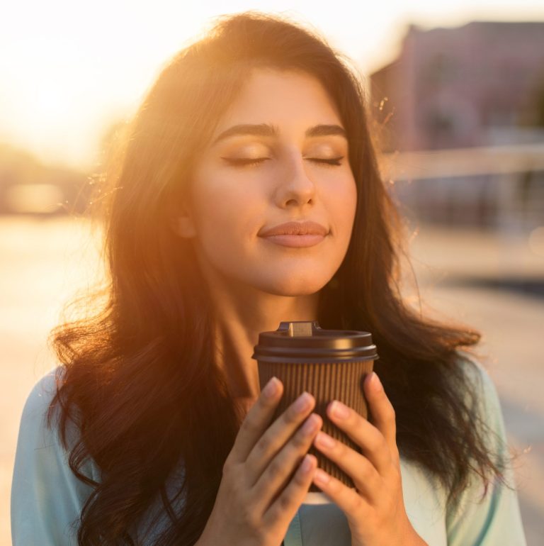 Woman with eyes closed enjoying a peaceful moment with a cup of coffee at SwitchYard.